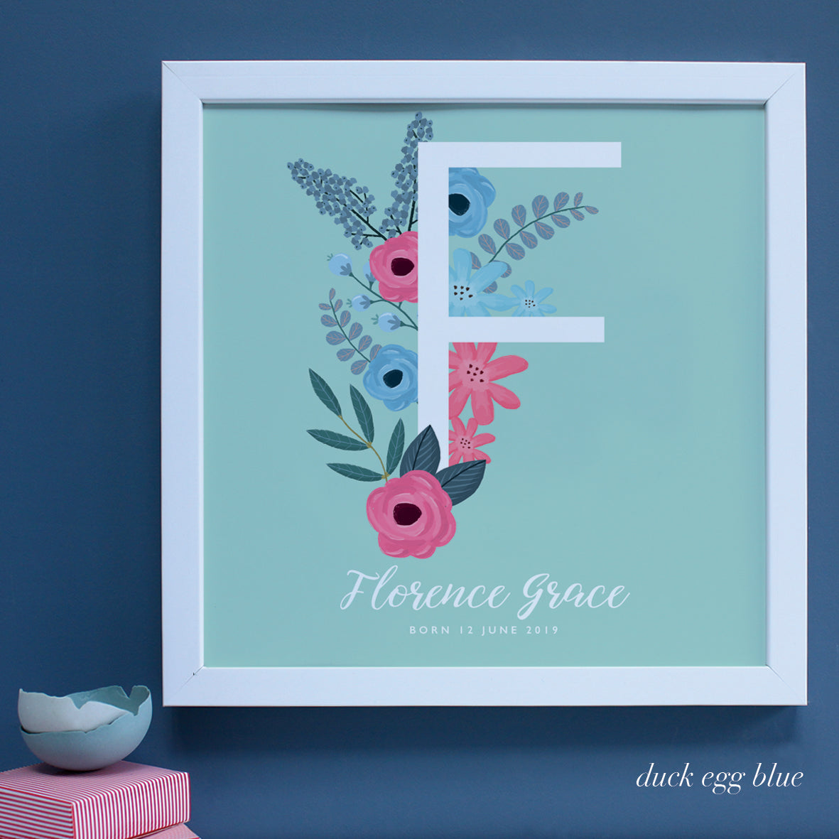 Large white framed New Baby present with letter F on duck egg blue background.